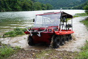 Red all-terrain vehicle with a canopy on a muddy path near a body of water.