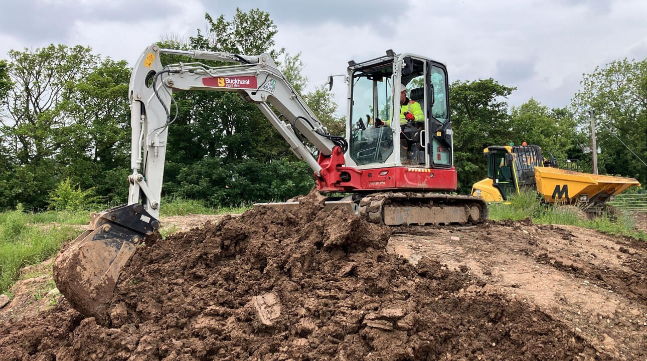 Red and white excavator digging into a pile of dirt with trees in the background