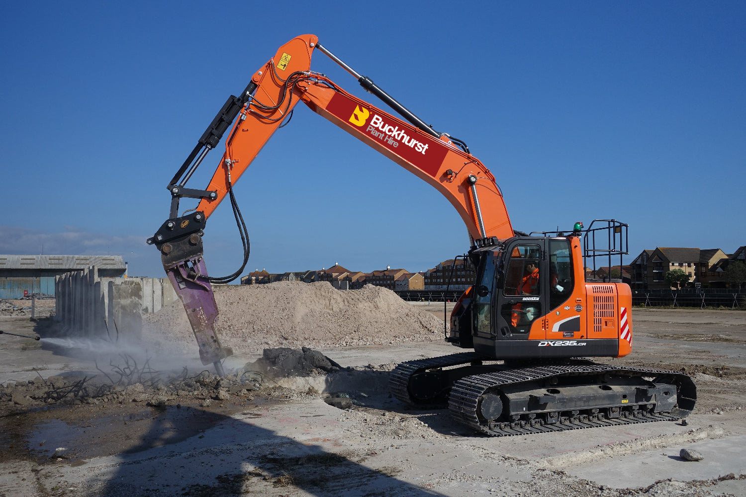 An orange Doosan 25T excavator with a demolition attachment is working on a construction site.