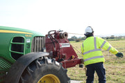 Person operating a tractor with a red attachment in a field