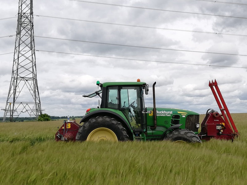 Green tractor in a field with power lines and tower in the background